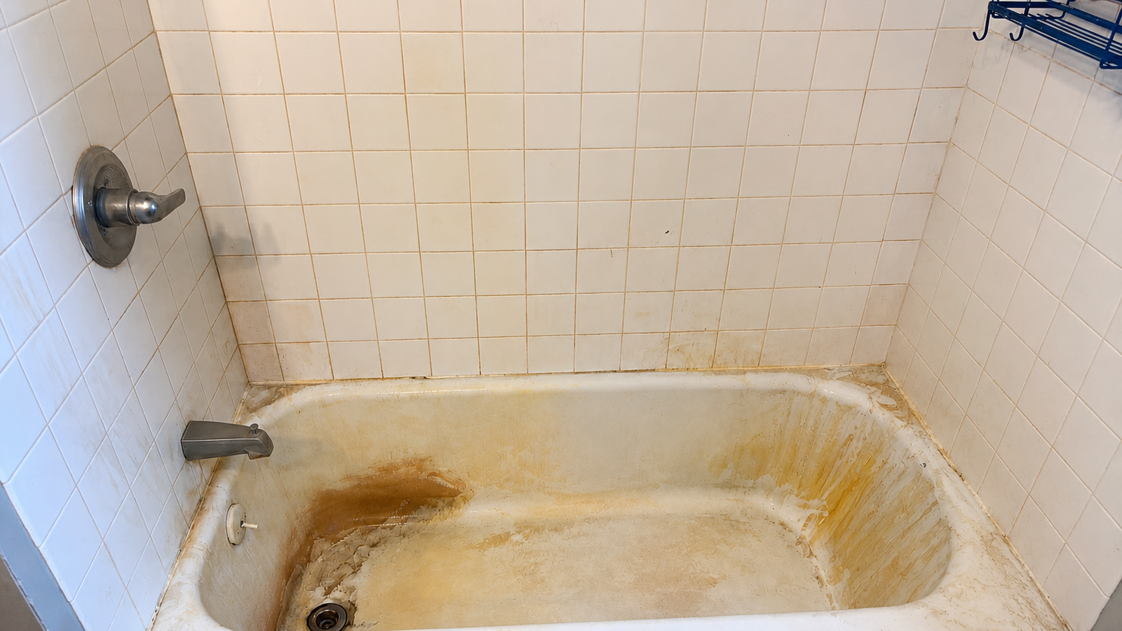 A bathtub and tile wall with heavy staining, rust marks and soap scum buildup.